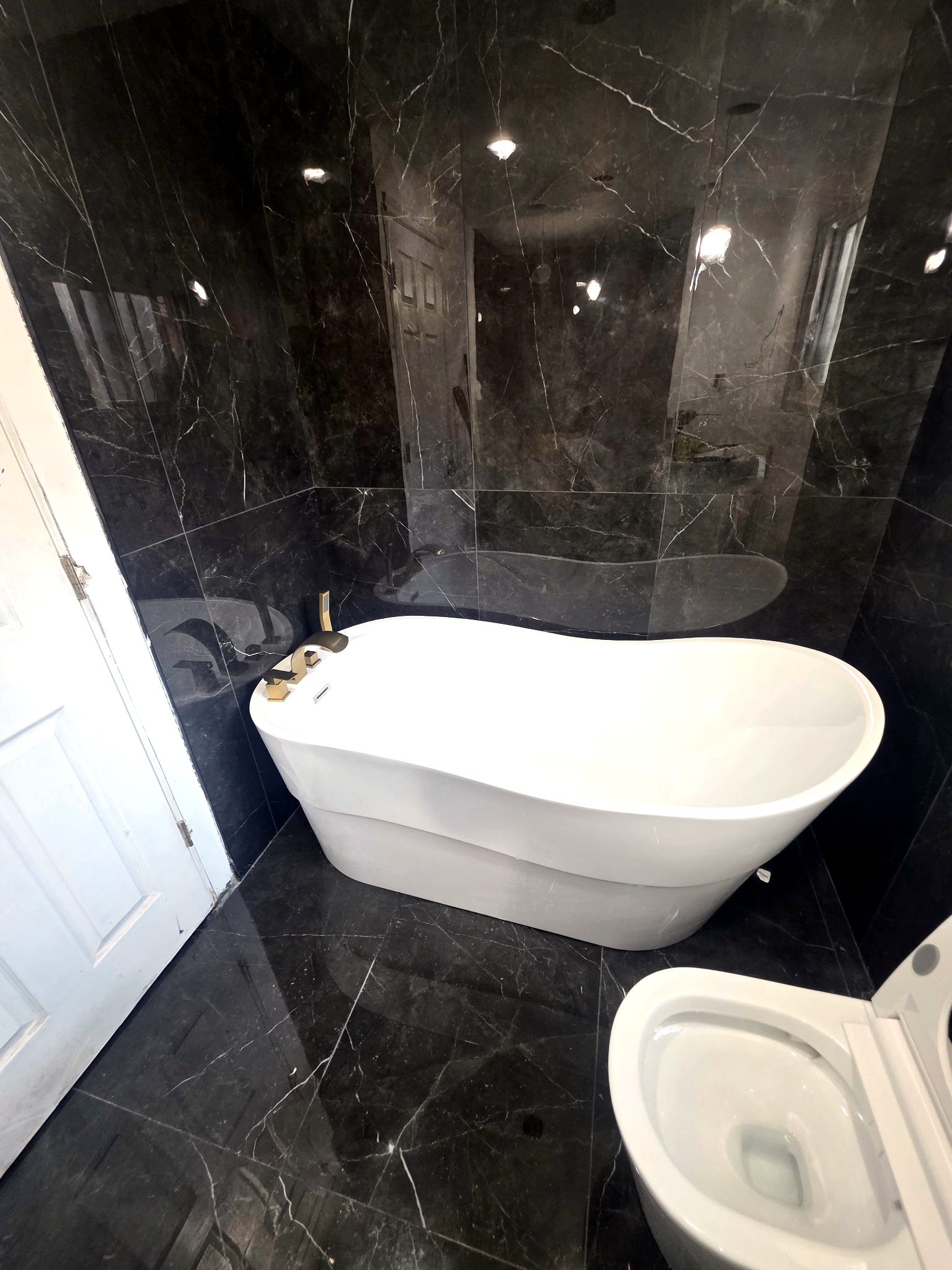 Freestanding white tub with gold fixtures against black marble tile