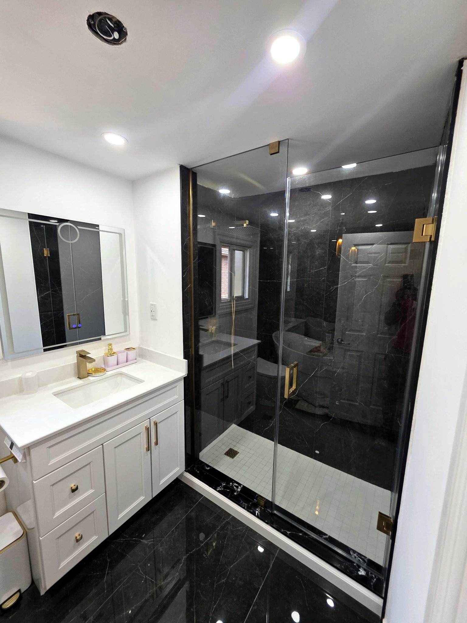 Renovated luxury bathroom with glass shower, black marble tile and gold trim